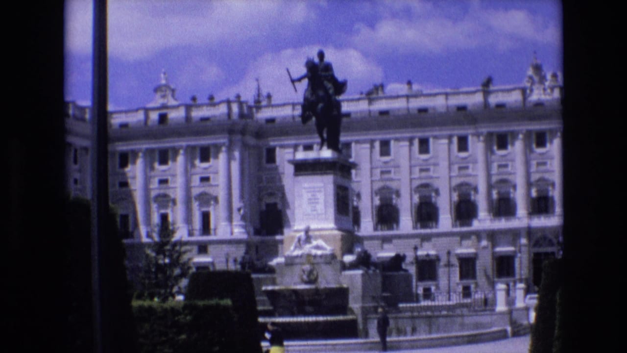 1972 Spain home-movie frame showing a grand palace facade, an equestrian statue on a pedestal, clipped greenery, and a fountain-like stone feature in the foreground.