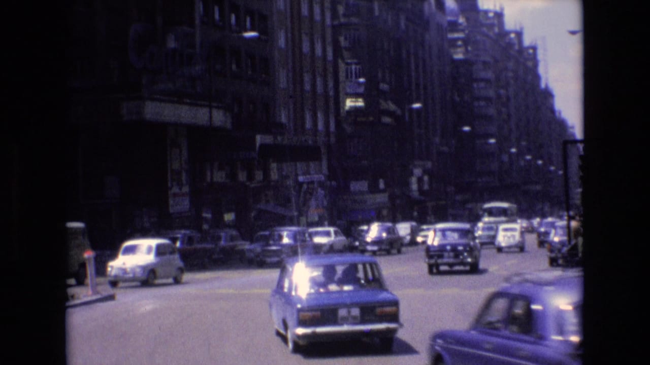 1972 Spain street scene with compact sedans and other cars moving along a broad avenue lined by tall buildings and commercial signage.