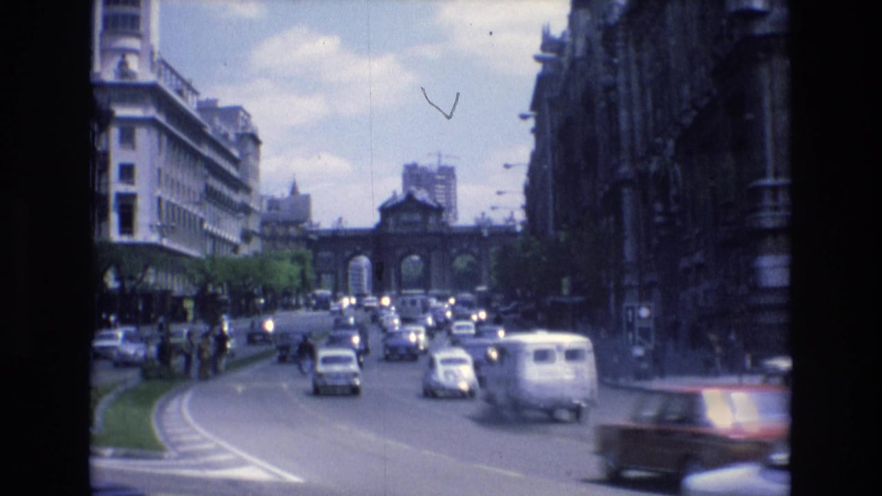 Cars and a white van travel along a broad street toward an arched structure.