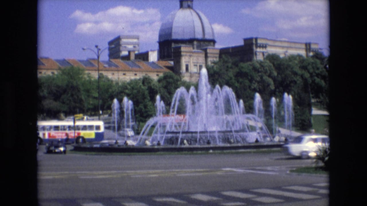 Large public fountain beside traffic with a domed building in the background.