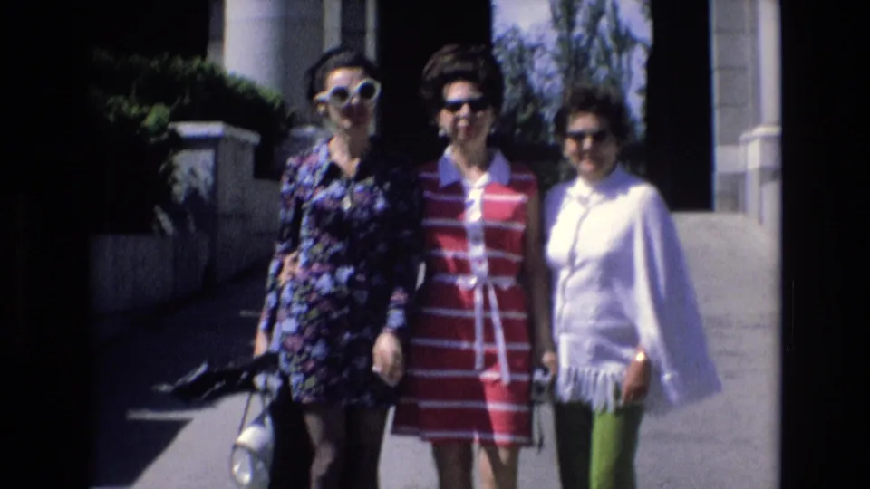 Spain 1972 8mm frame showing three women posing together near a columned building, including one in a floral dress, one in a red and white striped dress, and one in a white top with green pants.