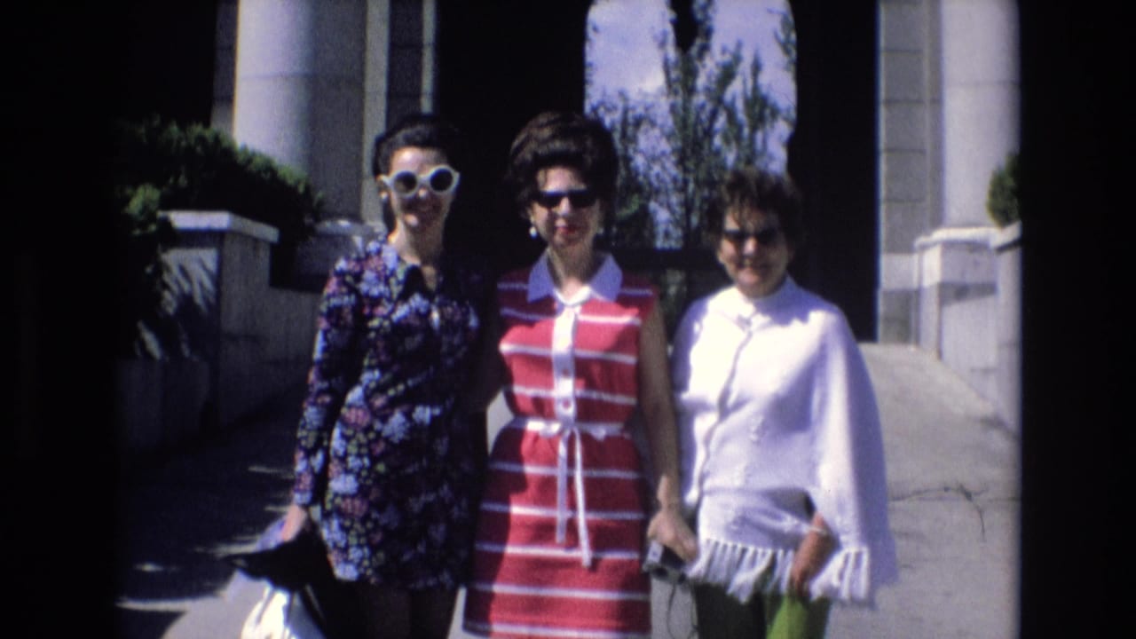 Three adult women in Spain in 1972 pose in sunglasses outside a building with columns and an arched entryway, wearing floral, striped, and fringed outfits.
