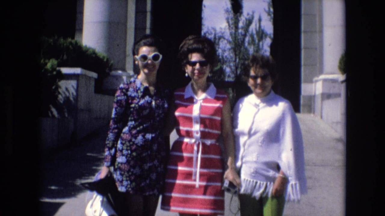 Three women stand smiling in bright sun near columns and a shaded doorway.