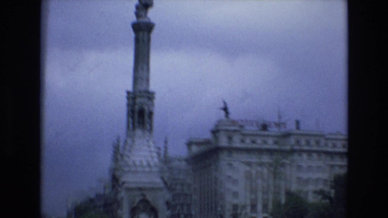 Tall column monument and neighboring multi-story building under cloudy sky.