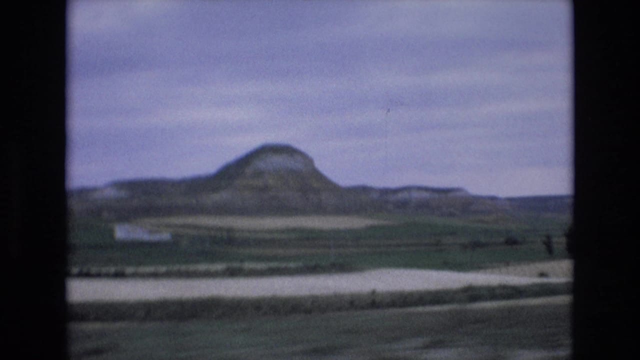 1972 8mm home-movie frame from Spain showing a rounded mountain rising beyond rural fields beneath a muted overcast sky.