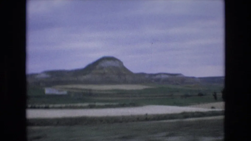 1972 8mm home-movie frame from Spain showing a rounded mountain rising beyond rural fields beneath a muted overcast sky.