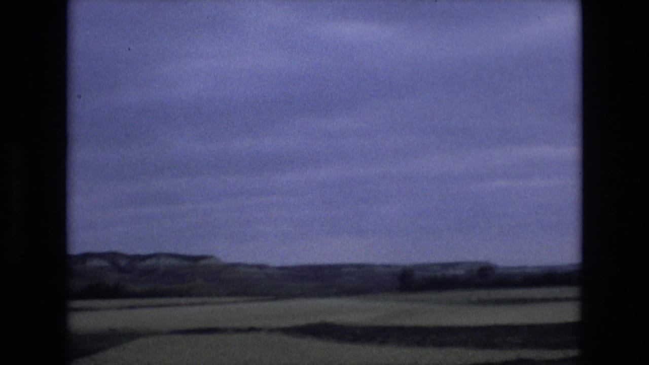 1972 Spain 8mm travel frame showing open green countryside and low distant plateaus beneath a blue, clouded sky.