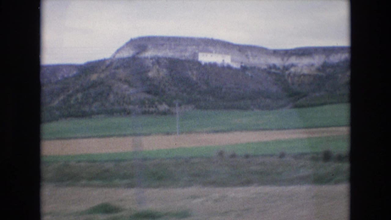 Rocky hillside with green fields below and a white building on the slope.