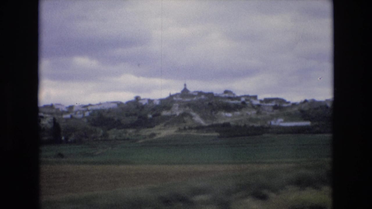 Hilltop town and fields viewed through dark train-window framing.