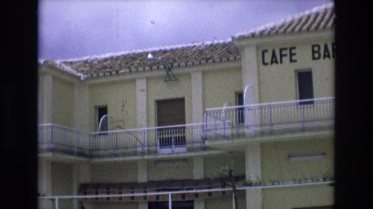 Spain 1972 home-movie frame of a pale yellow two-story cafe bar building with tiled roof, balcony railings, shuttered windows, and partial CAFE BAR lettering.