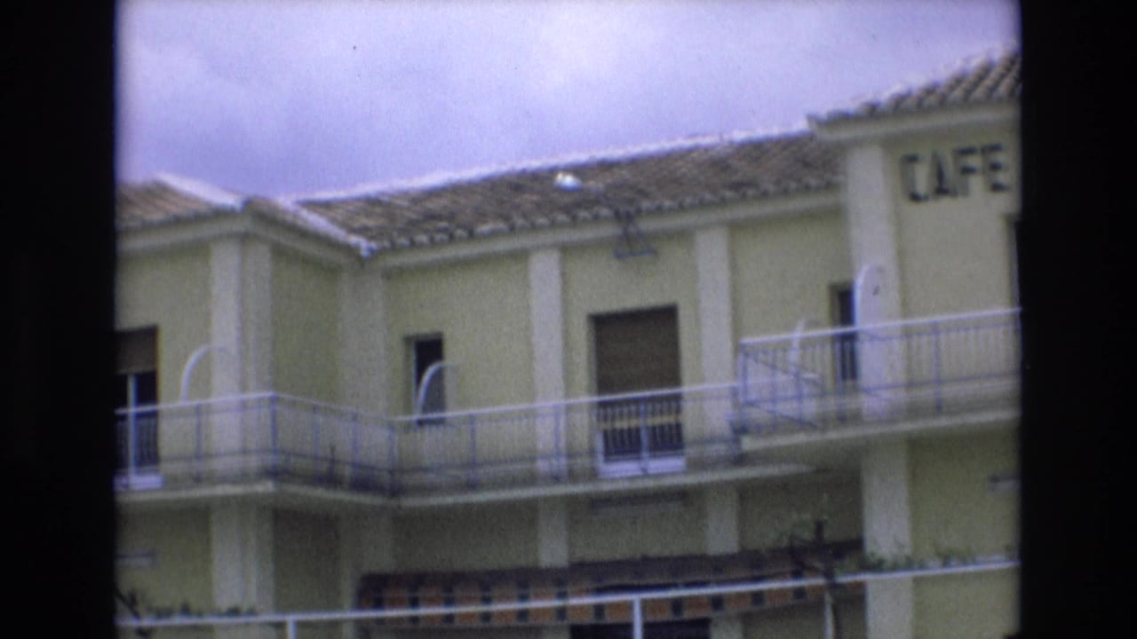 Upper facade of a yellow building with balcony railings and partial cafe sign.