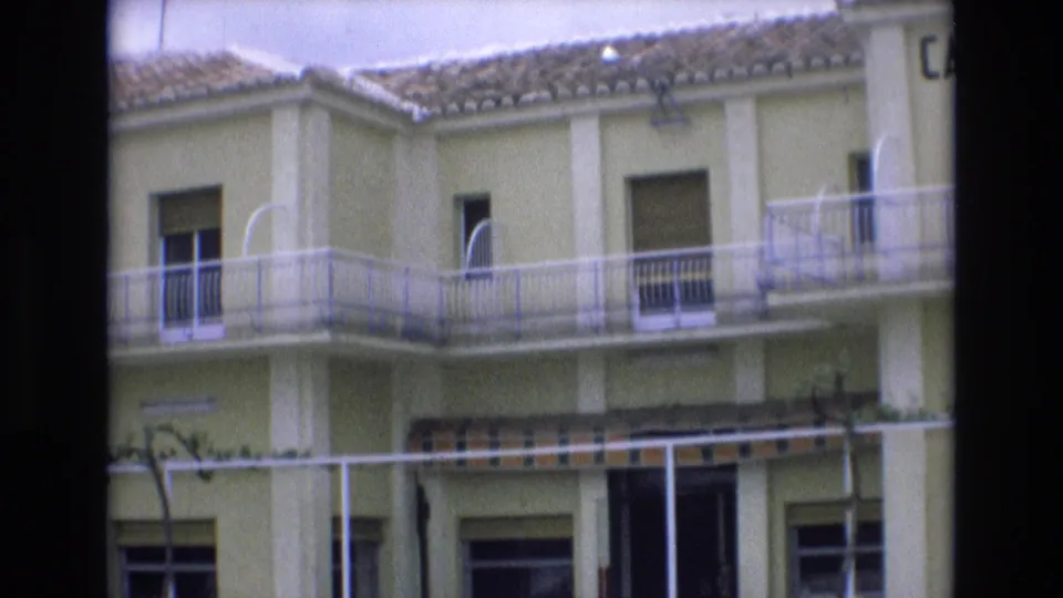 Spain 1972 home-movie view of the same yellow cafe bar exterior, showing balcony railings, shuttered windows, tiled roof, and the lower awning frame.