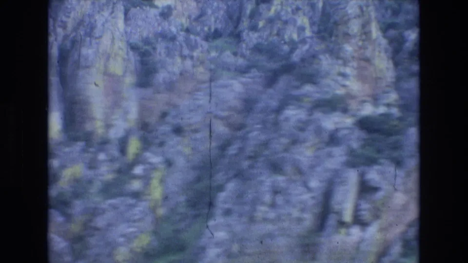 Soft, blurred 1972 Spain home-movie frame of rocky mountain terrain or hillside vegetation, with visible film scratches and blue-purple color shift.