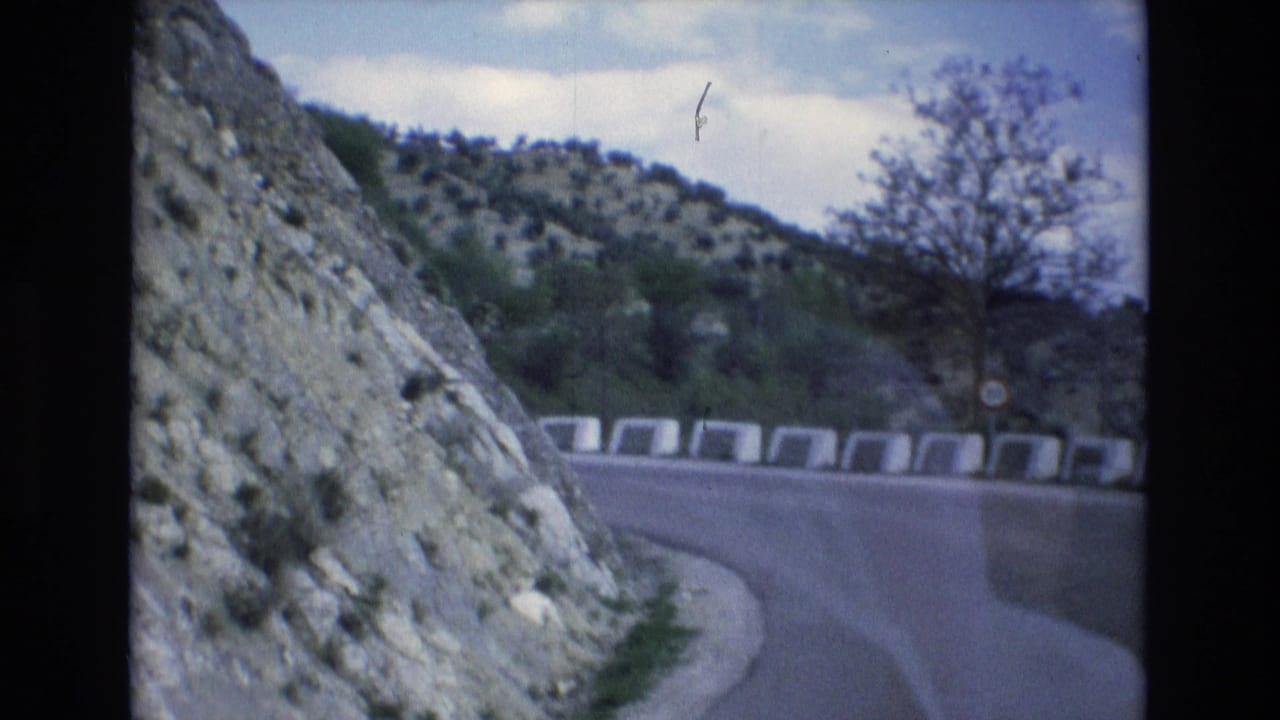 Winding road curves past a rocky cut slope with hillside vegetation beyond.