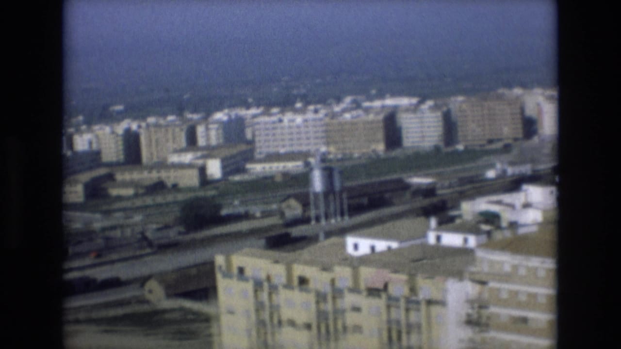 Urban rail corridor with apartment blocks and industrial-looking rooftop structures.