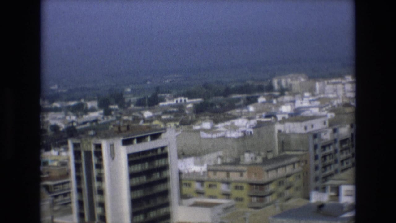 Elevated 1972 Spain home-movie view across mid-rise apartment blocks, flat rooftops, balconies, and a hazy distant horizon.
