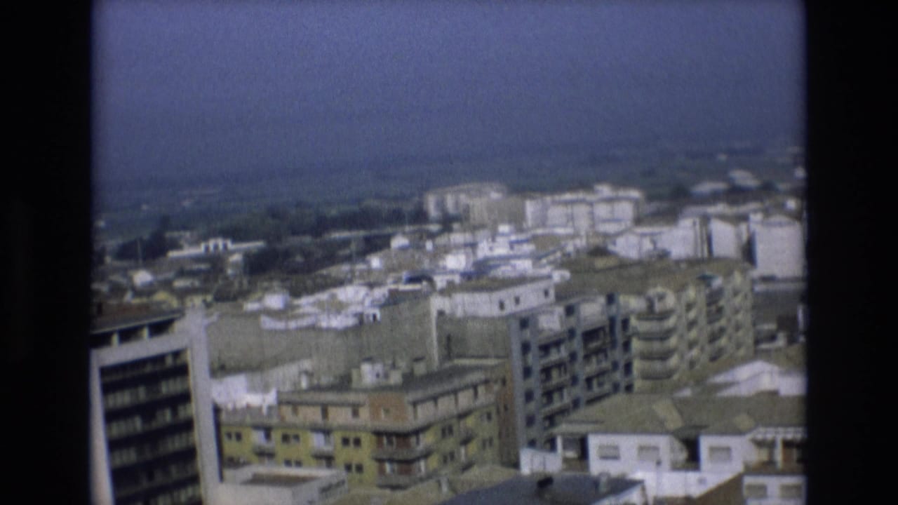Urban skyline with apartment blocks, rooftops, and a hazy background.