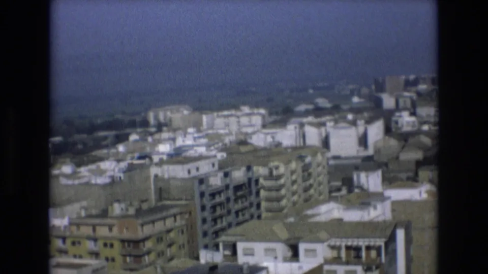 Elevated 1972 Spain home-movie frame with residential blocks, balconies, pale rooftops, and a hazy city edge in the distance.