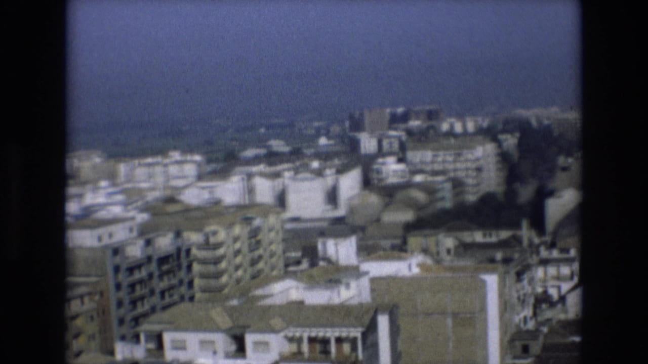 Soft 8mm frame from Spain showing a distant cityscape with apartment blocks and water on the horizon.