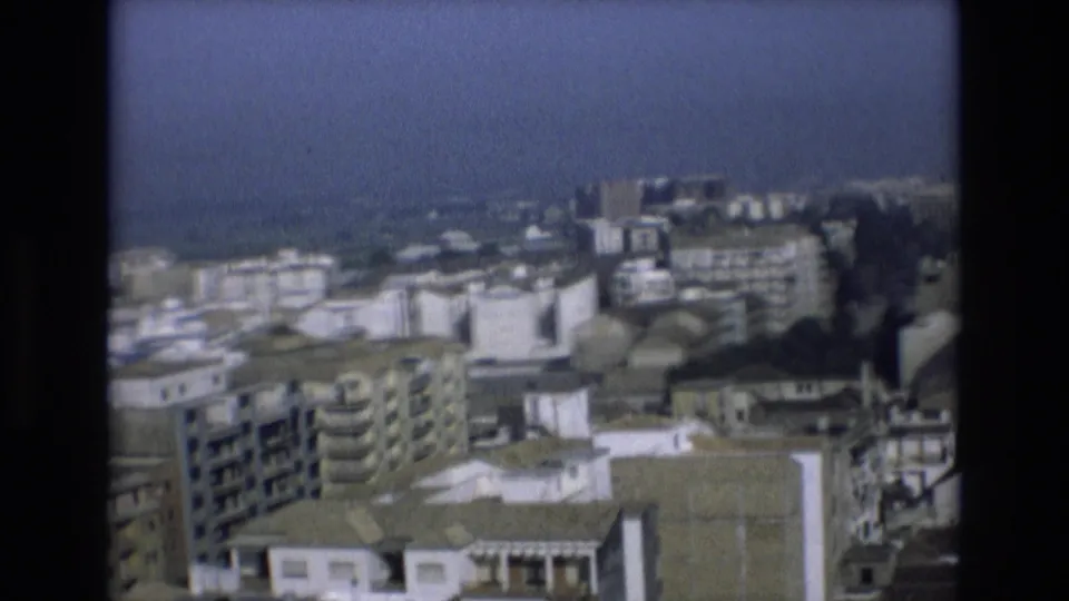 Soft 8mm frame from Spain showing a distant cityscape with apartment blocks and water on the horizon.