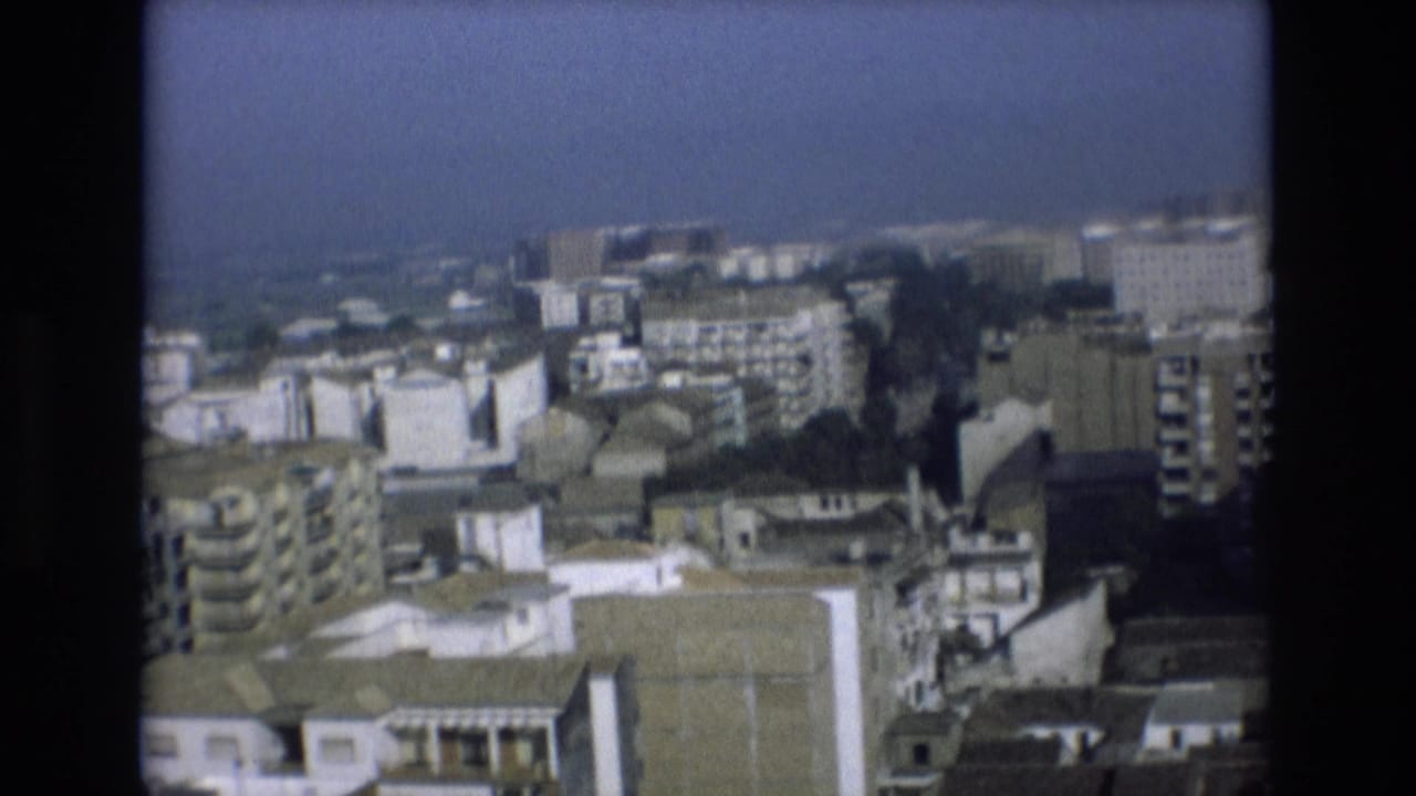 Distant cityscape with buildings, rooftops, and water in the background.