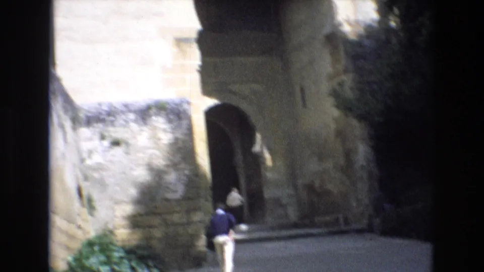 The home-movie camera turns to a historic stone passage in Spain, where a person is seen near an arched opening and pale masonry walls.