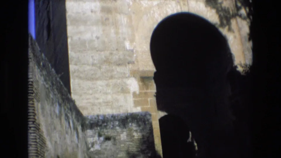 1972 Spain 8mm frame showing a silhouetted person near a dark arched doorway within weathered stone walls at a historic site.