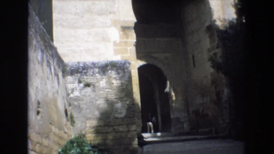 1972 Spain 8mm frame looking through a shadowed stone passage toward an arched opening and sunlit masonry beyond.