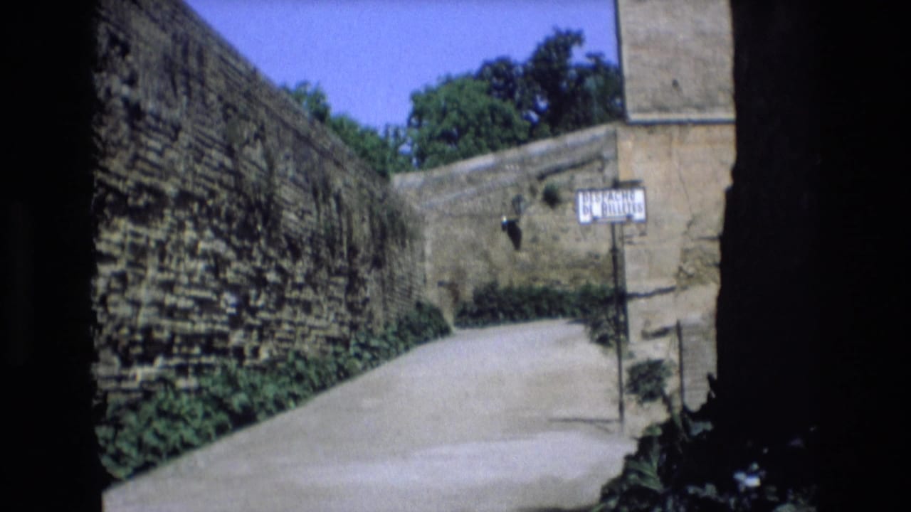 Sunlit stone-walled lane with a street sign near the far wall.