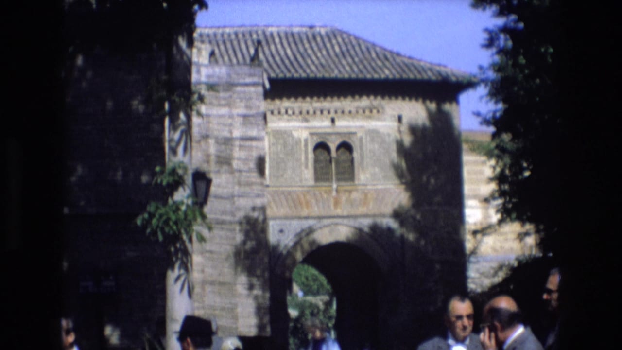 Stone entrance framed by trees with several men standing at the lower right.