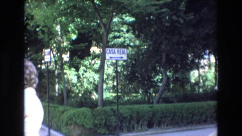 1972 Spain 8mm frame repeating the visitor's view of a "CASA REAL" sign beside hedges and dense trees, with a person partially entering the left side of the frame.