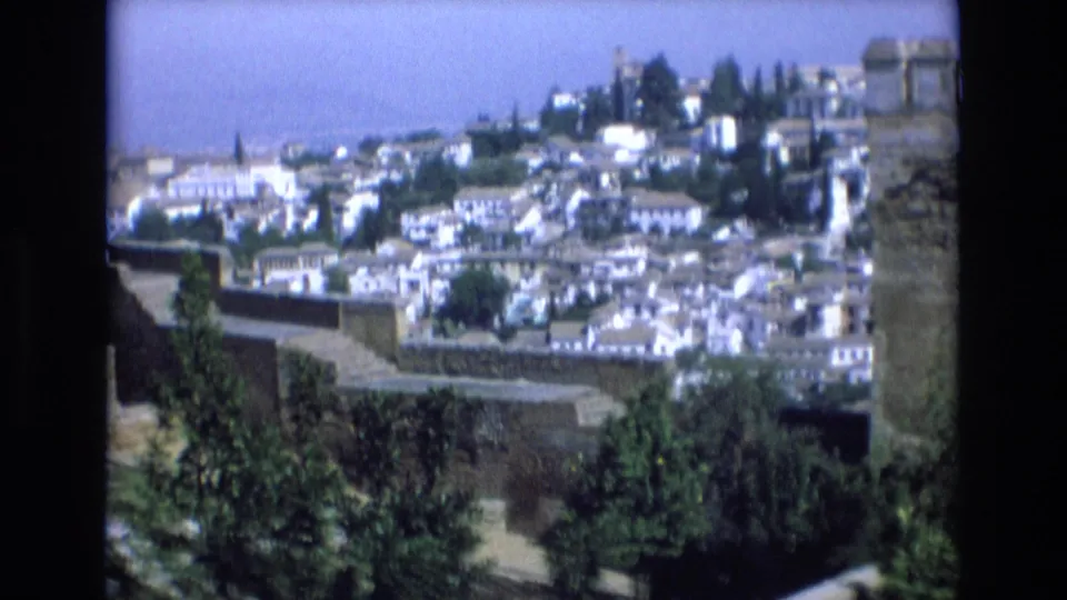 1972 Spain 8mm frame showing an elevated panorama of a traditional town with white buildings, hillside greenery, and distant rooftops under bright daylight.