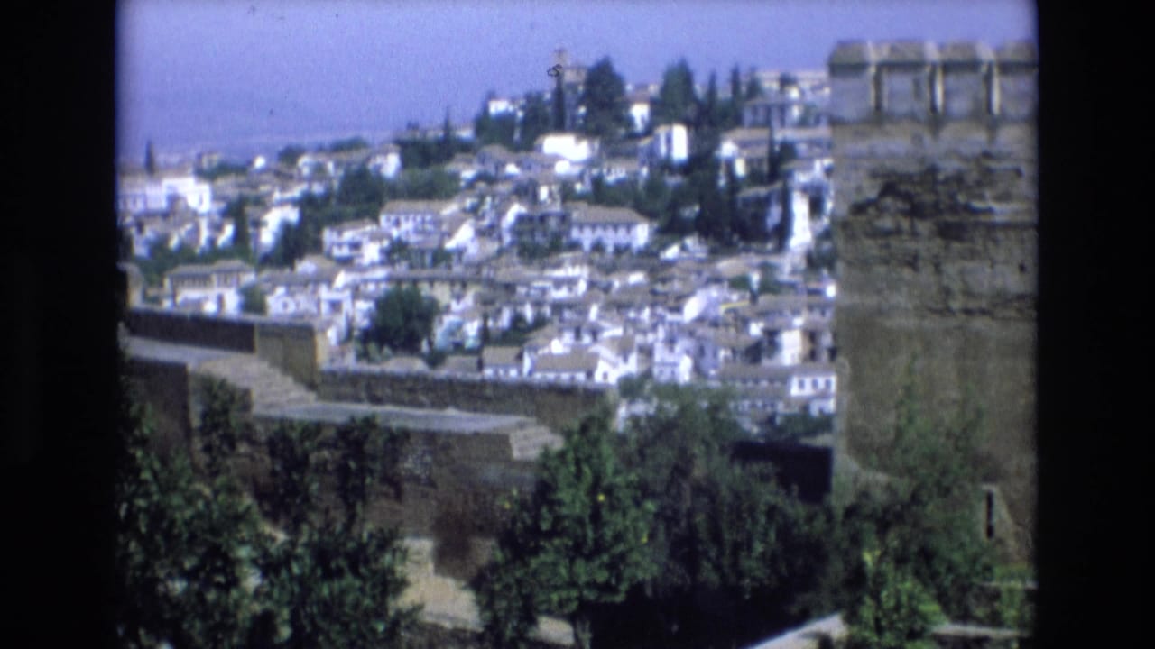 1972 Spain 8mm frame showing a panoramic hillside town of white buildings behind a large stone fortress wall and crenellated turret.