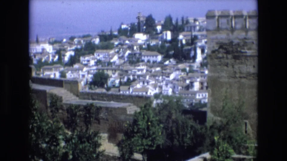 1972 Spain 8mm frame showing a panoramic hillside town of white buildings behind a large stone fortress wall and crenellated turret.