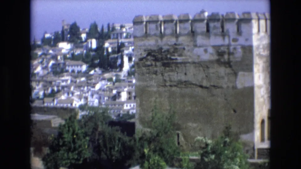 1972 Spain 8mm frame with a prominent crenellated stone turret in front of a dense hillside town and scattered trees.