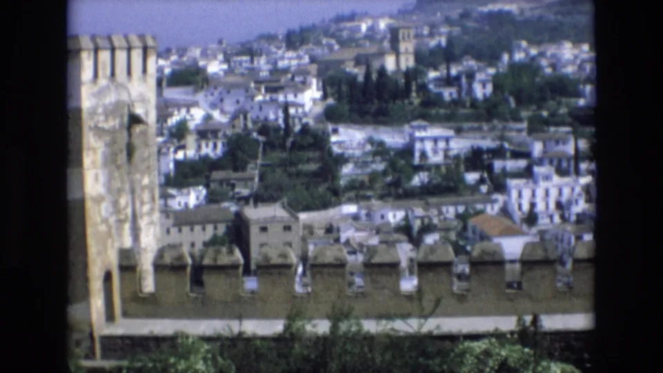 1972 Spain 8mm frame with a masonry wall in the foreground and a sunlit town of white buildings rising across the hillside.