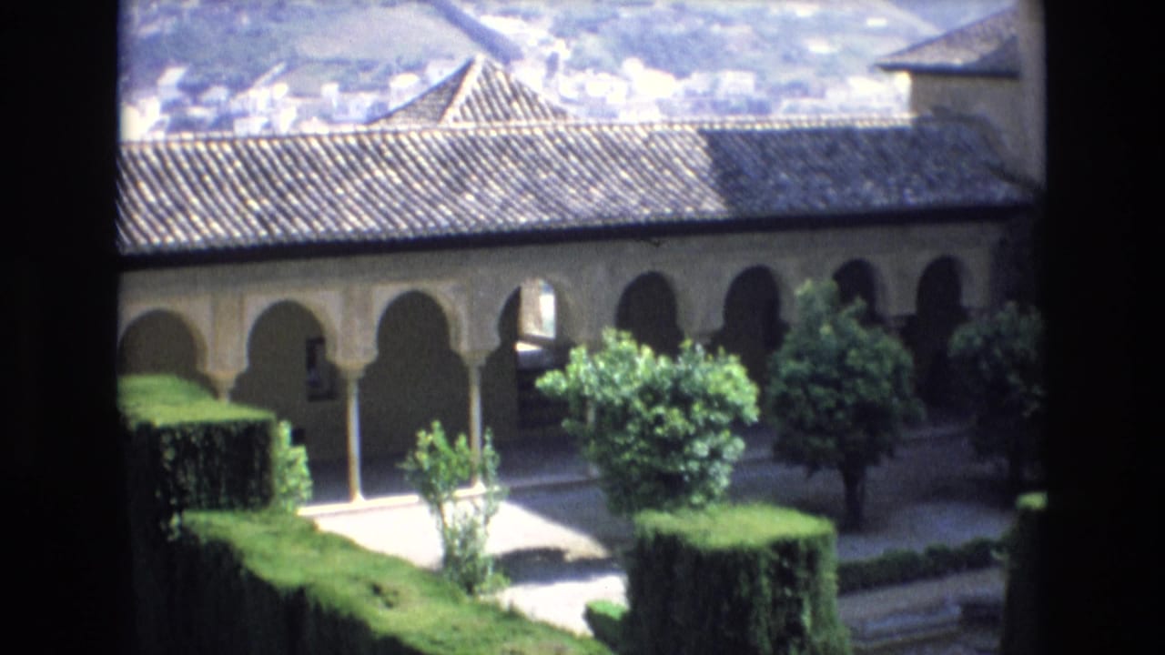 1972 Spain 8mm frame showing a Moorish-style arched arcade above a formal courtyard garden with hedges, paths, and small trees, seen from a dark window or balcony edge.