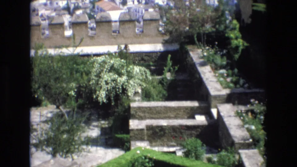 Elevated 1972 Spain view across a walled garden courtyard, with small trees, planted beds, stone paths, and rooftops beyond.