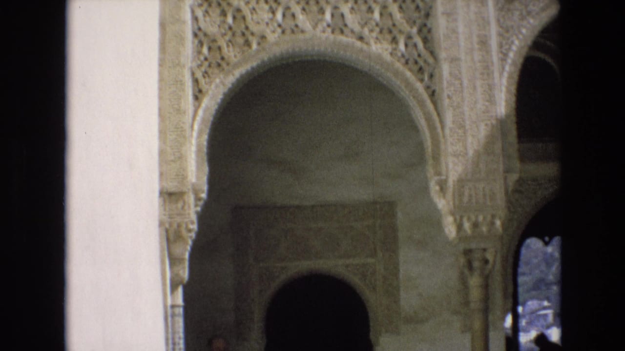 1972 Spain 8mm frame showing a historic interior with Moorish-style arches, carved stucco ornament, pale walls, columns, and deep shadowed openings.