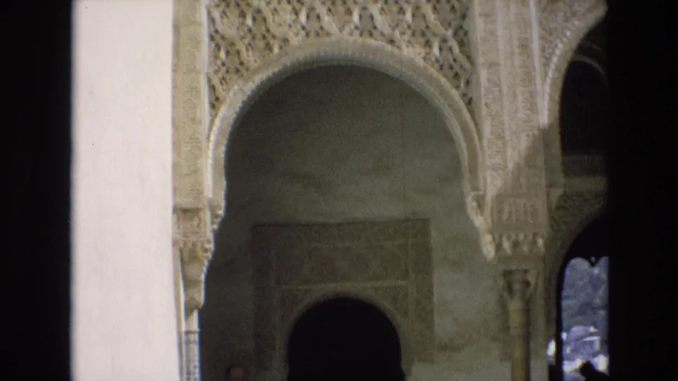 1972 Spain 8mm frame showing a historic interior with Moorish-style arches, carved stucco ornament, pale walls, columns, and deep shadowed openings.