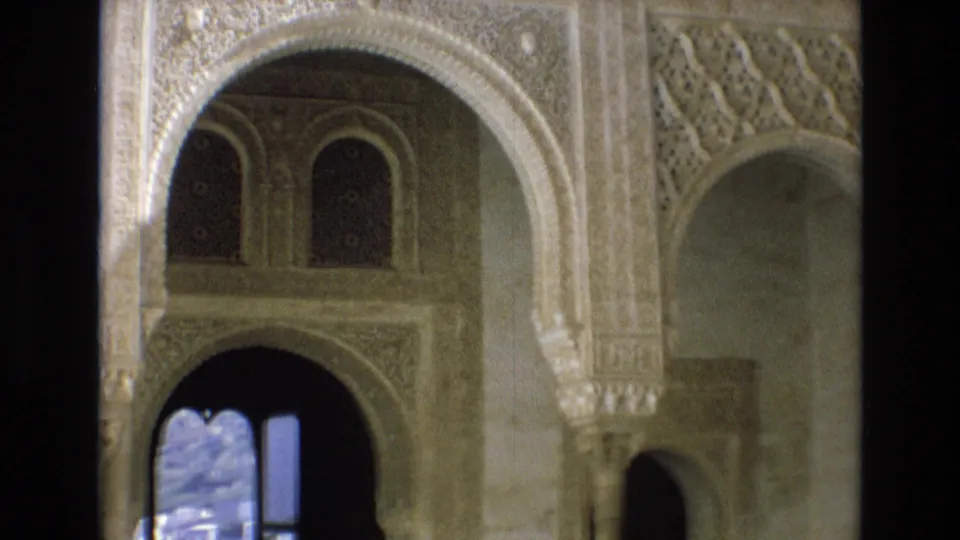 1972 Spain 8mm frame of a historic interior with a large carved arch, patterned stucco, upper arched windows, dark doorway space, and pale wall surfaces.