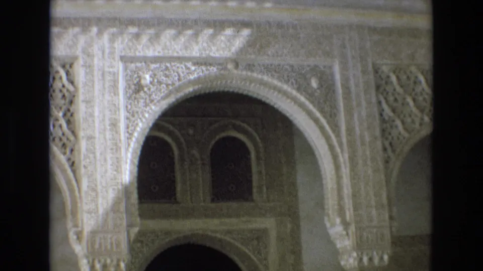 1972 Spain 8mm frame showing an ornate horseshoe arch with carved decoration, shadowed windows, and Moorish-influenced interior architectural detail.