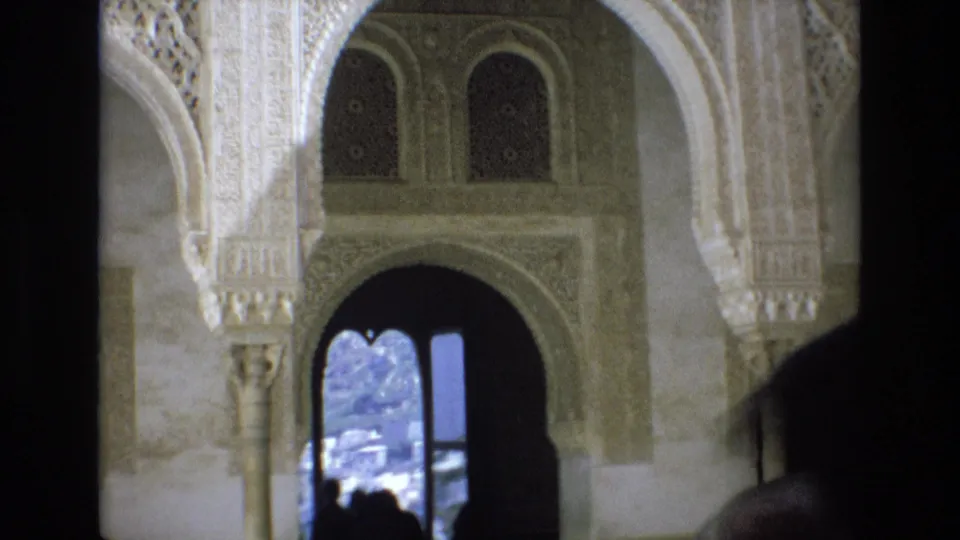 1972 Spain 8mm frame showing a close visitor-shot view of Moorish-style palace ornament, arched openings, and shadowed figures near a bright exterior doorway.