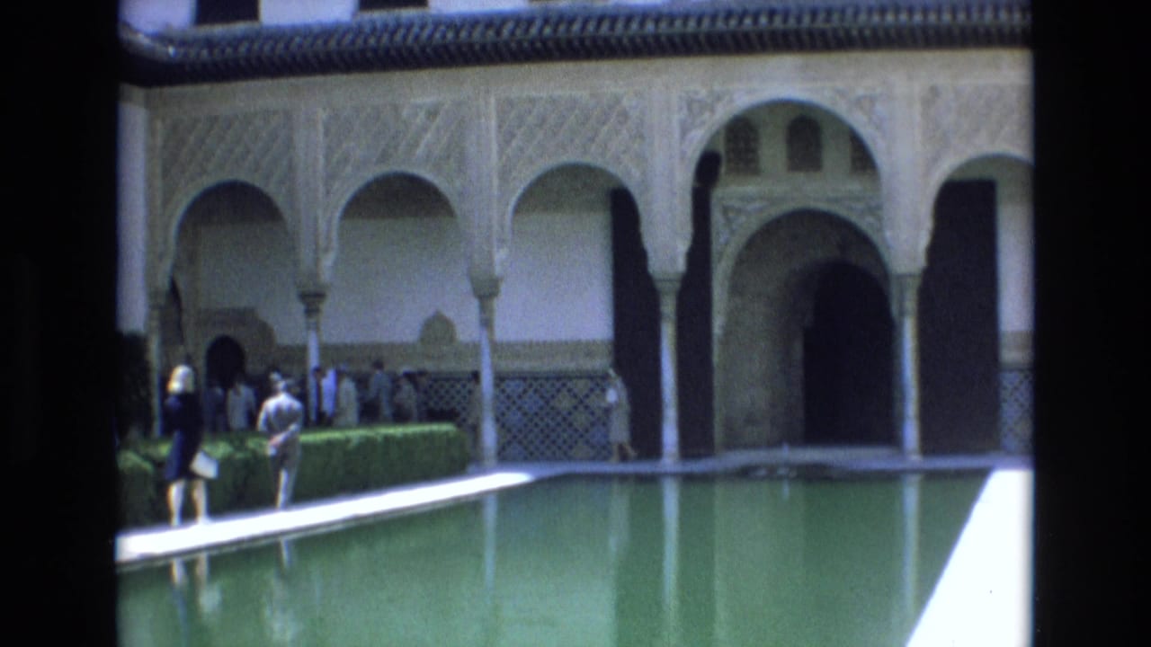 1972 Spain travel footage shows adult visitors beside a green reflecting pool under Moorish-style courtyard arches and patterned wall tilework.