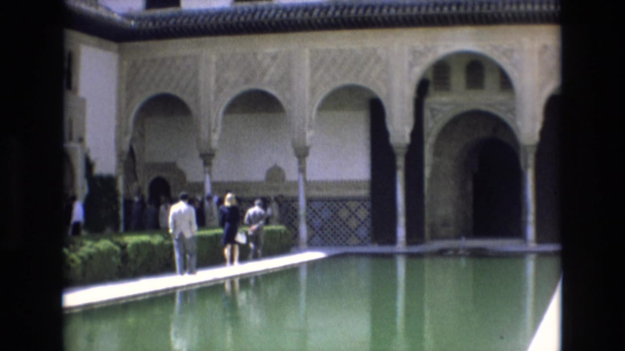 In metadata-supported 1972 Spain, tourists stand and walk along a reflecting pool beneath Moorish-style arches and carved wall decoration.
