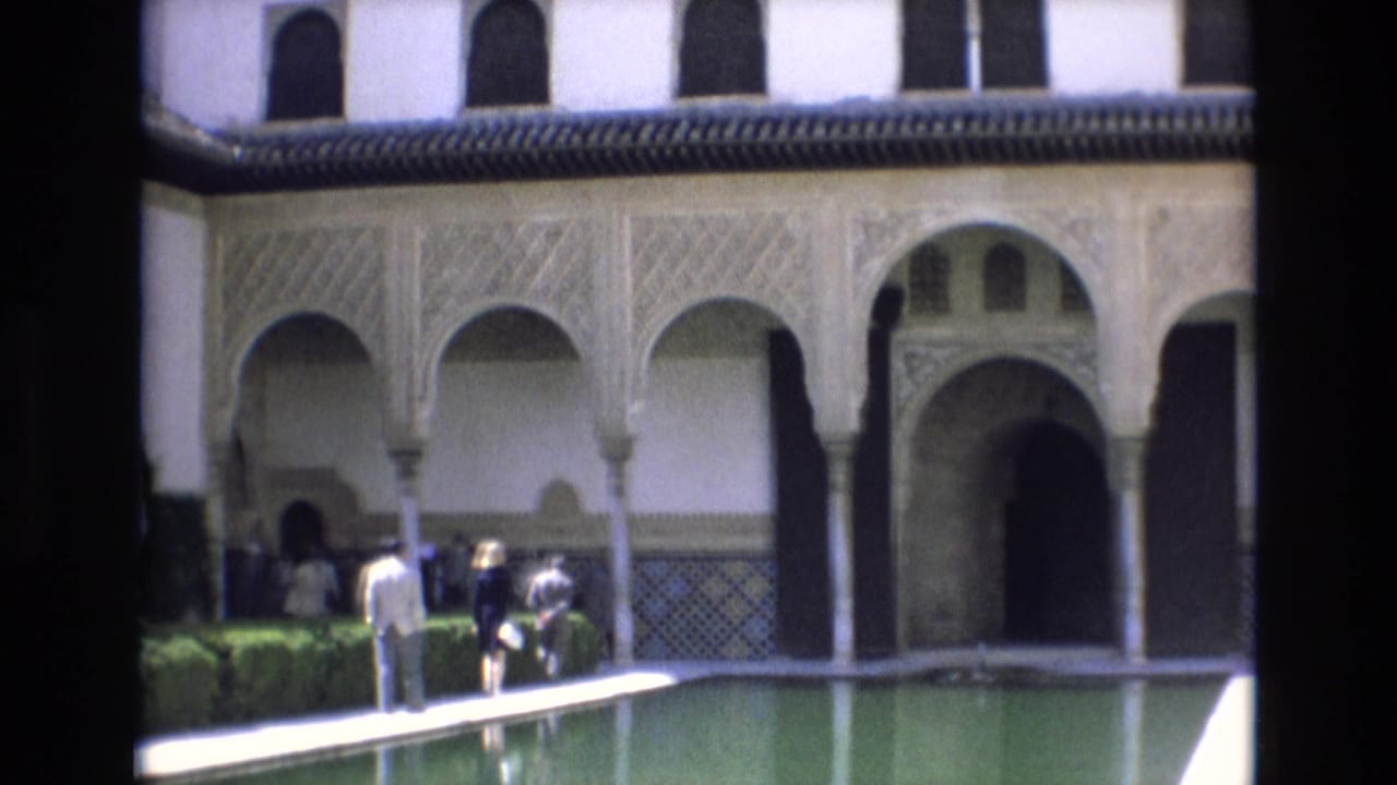 Several visitors gather near hedges beside the pool and arched building facade.