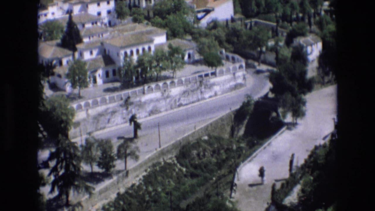 White buildings and trees above a stone wall with a road and pedestrian path below.
