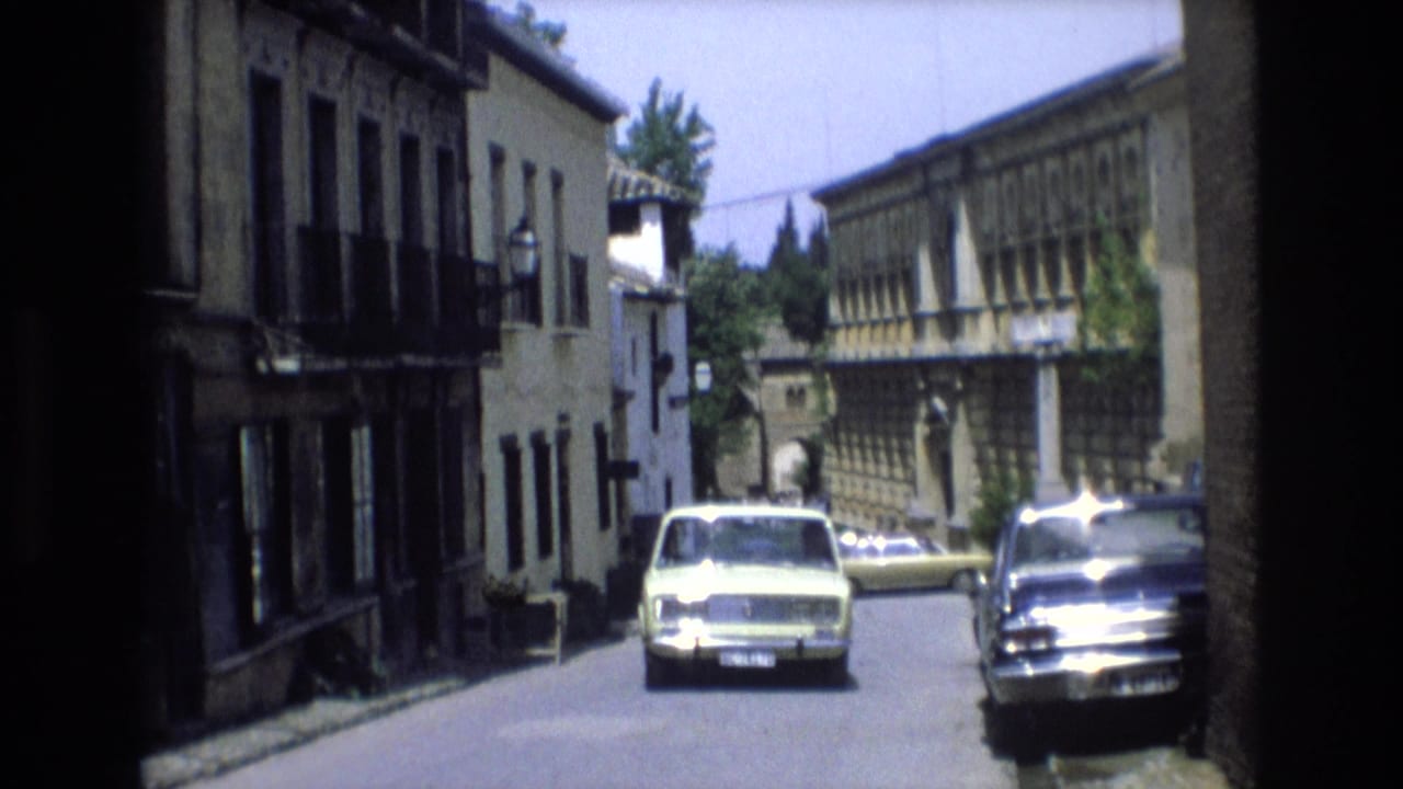 Classic car nearing the camera while a dark sedan is parked along the right side of the street.