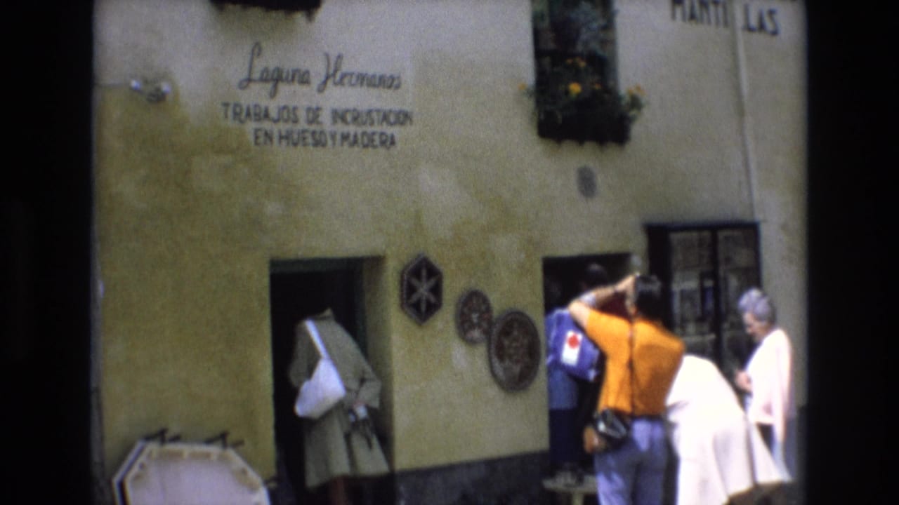 In Spain in 1972, adult tourists gather at the entrance of a stucco-fronted Laguna Hermanos workshop with a painted sign and decorative wall pieces visible.