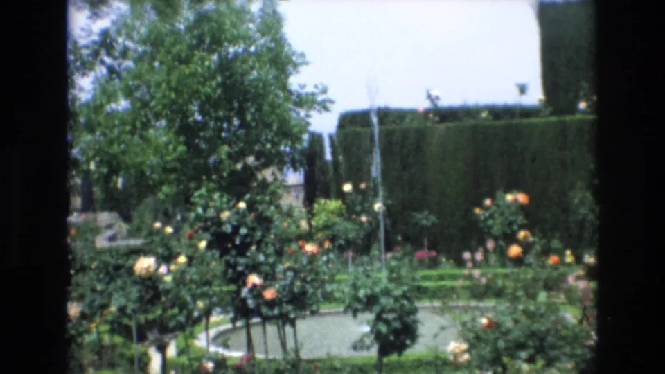 A lush Spanish garden scene shows rose bushes, a small fountain or pool, tall hedges, trees, and bright sky within the same 1972 travel footage.